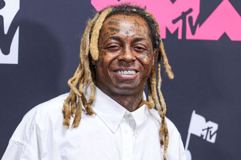 Lil Wayne smiling in press photo wearing a hat and sunglasses